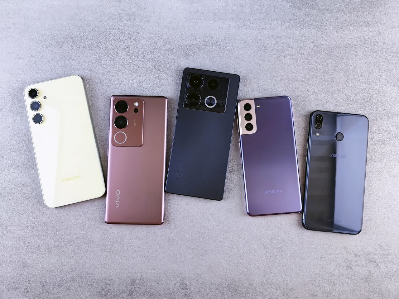 Home Flat lay of five modern smartphones on a gray surface, showcasing various designs.