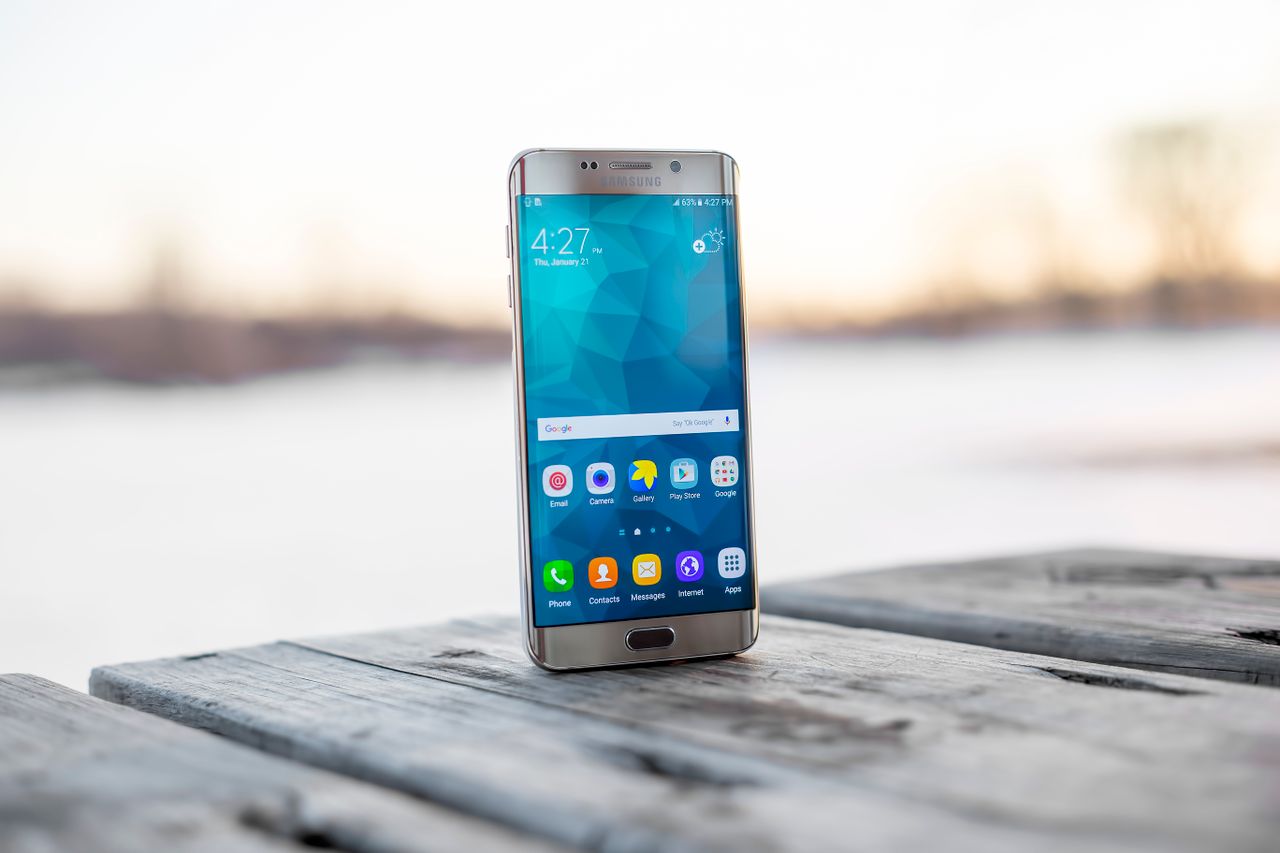 Home Samsung smartphone placed on a wooden surface outdoors during sunset.